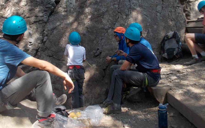 a teen belays during a rock climbing exercise while several others look on